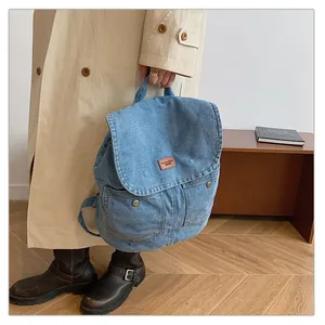 Detail of light blue denim backpack showing leather label and pocket buckles in lifestyle view