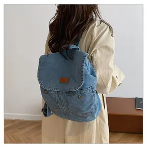 Detail of blue denim backpack showing wash texture and leather logo patch on flap