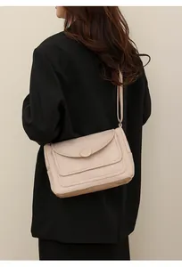 Dettaglio della borsa a tracolla in pelle beige con patta arrotondata e fibbia sul modello