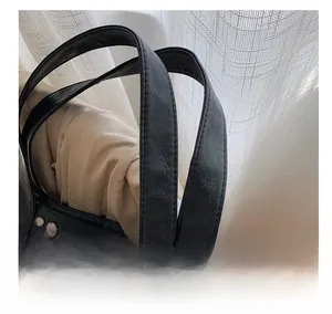 Detail of soft leather handle and silver stud rivets on black tote bag with stitching