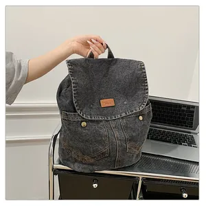 Detail of washed denim backpack featuring front pockets and brown leather logo patch