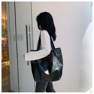 Detail of black tote bag with silver studs worn by a model against a white wall