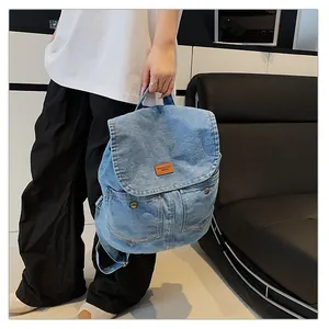Detail of light blue denim backpack showing brown leather label and metal buckle pockets