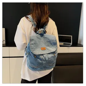 Light blue denim backpack with flap cover and brown leather patch in a casual school style
