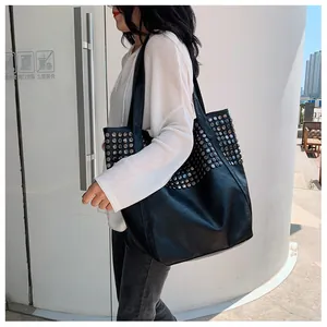 Close-up of black studded tote bag with silver rivets worn over shoulder by a model