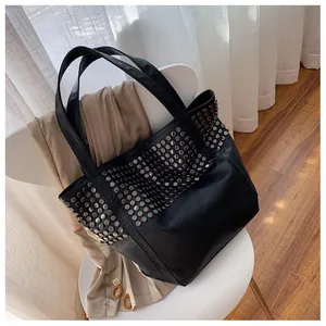 Detailed view of large black tote bag with silver rivets on a white chair background