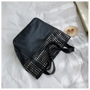Close-up of black leather tote bag with silver metal studs on a white fabric background