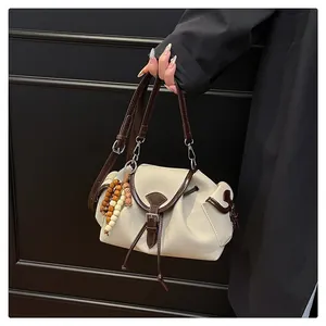 Detail of beige canvas bucket bag with brown leather trim and colorful wooden bead charm