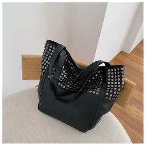 Detailed close-up of a black faux leather tote bag with silver metal rivet studs decoration