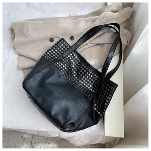 Top view of large black tote bag with silver studs on soft white fabric background