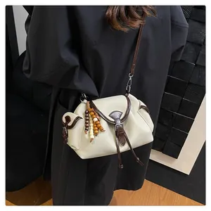 Detail of beige bucket bag with dark brown leather trim and colorful beaded tassel charm