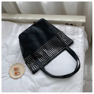 Close-up of black rivet tote bag with silver metal studs and grainy leather texture