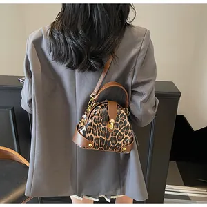 Leopard print shell handbag with gold studs and brown leather trim on model