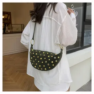 Detail of dark green suede saddle bag featuring golden rivets and metal ring accents