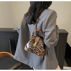 Close-up of leopard print shell bag with brown leather trim and golden metal clasp