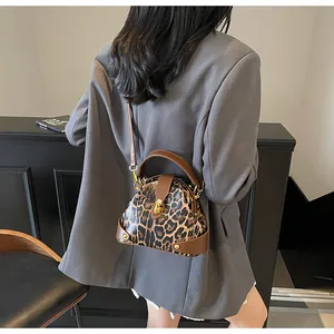Detail of leopard print shell bag featuring a gold twist lock and brown leather strap