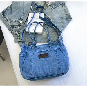 Detail view of denim tote bag featuring brown leather patch and adjustable shoulder strap