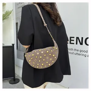 Close-up of taupe half-moon suede bag with gold eyelet studs and adjustable strap