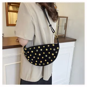 Detail of a black hobo bag with gold rivets and grommets on a model's shoulder