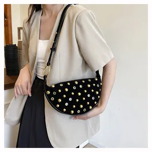 Detail of black suede crescent bag with gold studs and metal eyelets on model