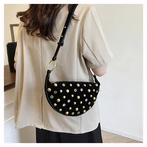 Detail of a black suede crescent bag with golden rivets and eyelets on a shoulder model