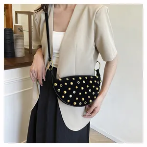 Detail of a black crescent bag with gold studs and eyelets on a crossbody strap