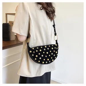 Detail of black suede crescent bag with gold metal eyelets and rivets on a model's shoulder