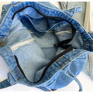 Detail view of denim tote bag showing interior lining, zipper closure and yellow stitching