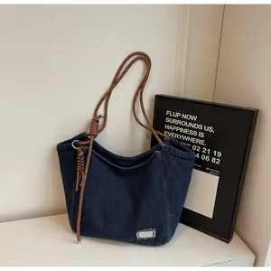 Detail of denim tote bag with thick rope straps and metal decorative plate detail