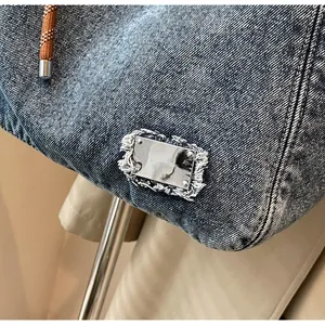 Detail of silver square metal tag on blue denim tote bag with frayed edges and woven handles