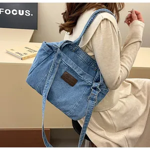 Detail of blue denim tote bag with leather logo tag shown on person's shoulder