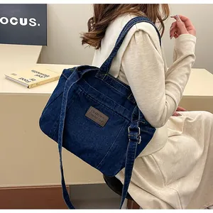 Detailed view of deep blue denim tote bag featuring leather badge and durable straps