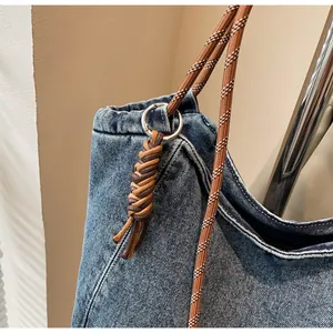 Close-up of blue denim tote bag with woven shoulder strap and silver metal ring connector