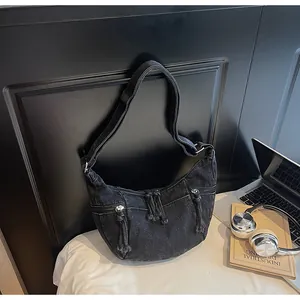 Detail of washed denim crescent bag with dual zipper pockets and adjustable wide strap