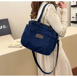 Detail of blue denim tote bag featuring a leather logo patch and side pocket storage