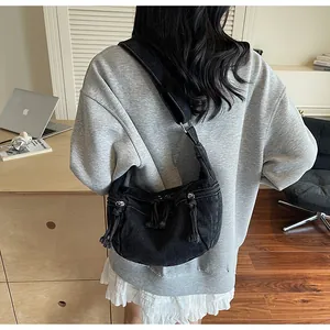 Close-up of black denim crossbody bag with fringe zipper detail worn with a casual outfit