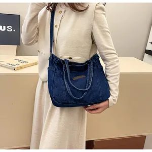 Detail of blue denim tote bag with leather patch and adjustable strap worn on shoulder