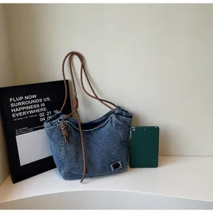 Detail of blue denim tote bag with brown braided rope handle and vintage frayed patch