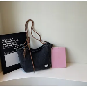 Macro detail of washed black denim tote bag with brown woven rope strap and white brand label