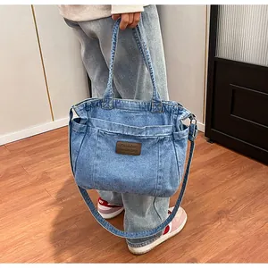 Detail view of a large denim tote bag featuring a brown leather fashion patch and side pocket