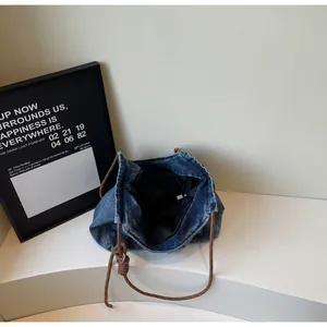 Detail of blue denim tote bag featuring brown woven rope straps and inner pocket