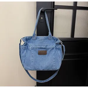 Detail of blue denim tote bag with brown leather patch and adjustable shoulder strap