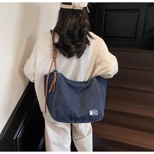 Detail of blue denim tote bag with knotted rope shoulder strap and silver accent patch