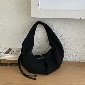 Λεπτομέρεια μαύρης σουέτ τσάντας hobo με πλαϊνούς κόμπους σε ξύλινο τραπέζι