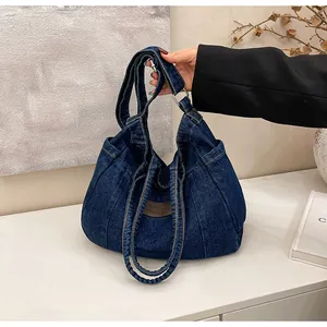 Detailed close-up of dark blue denim tote bag with leather logo and metal ring strap