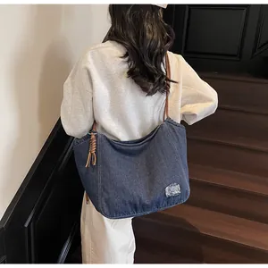 Detail of dark blue denim tote bag featuring brown woven rope handles and side tassel