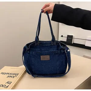 Detail of dark blue denim tote bag with leather tag and adjustable shoulder strap