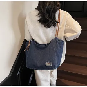 Rear view of a blue denim hobo bag with an orange woven rope strap worn over the shoulder