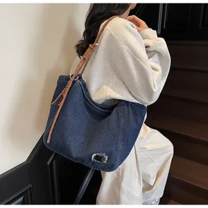 Detail of deep blue denim tote bag featuring woven rope strap and distressed patch
