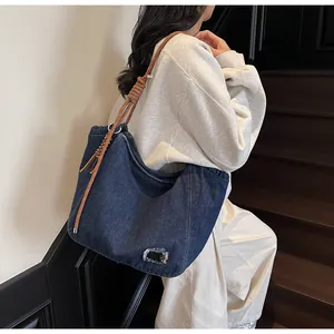 Detail of denim tote bag featuring brown woven rope shoulder strap and frayed fabric patches